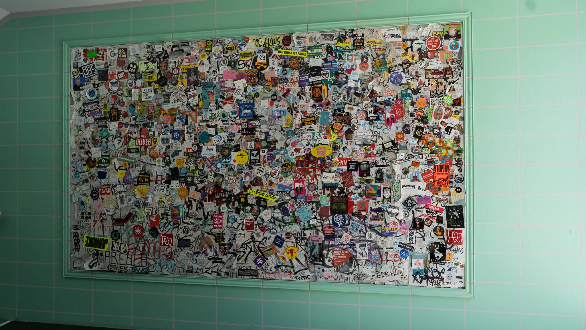 A tiled wall with a framed panel covered in hundreds of stickers