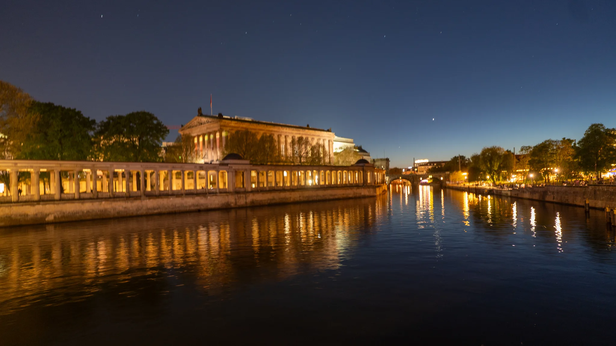 The colonnades of Museum Island lit up at night and reflected in the River Spree