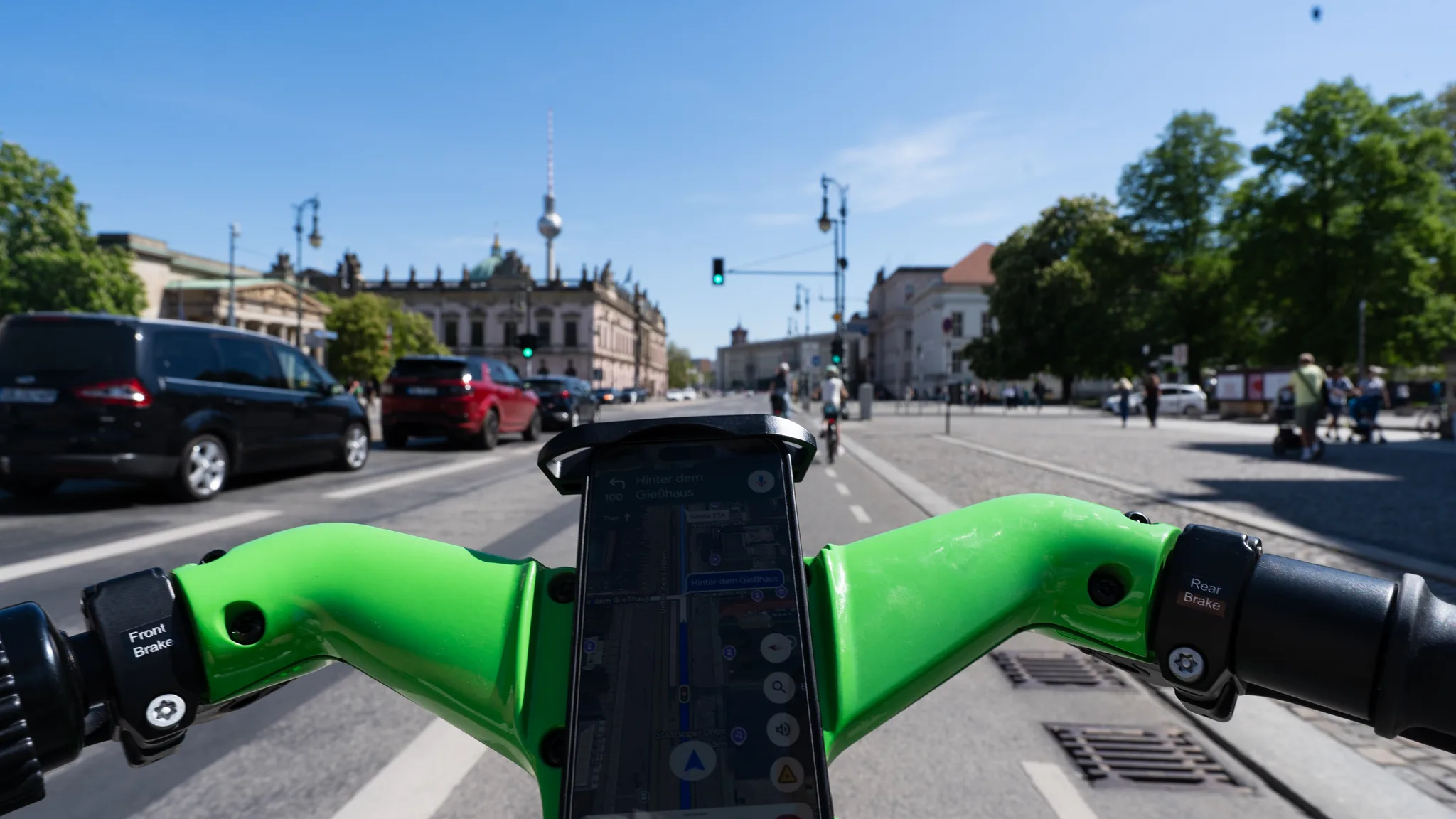 A wide Berlin avenue with the TV Tower in the distance, seen over the handlebars of a green hire bike