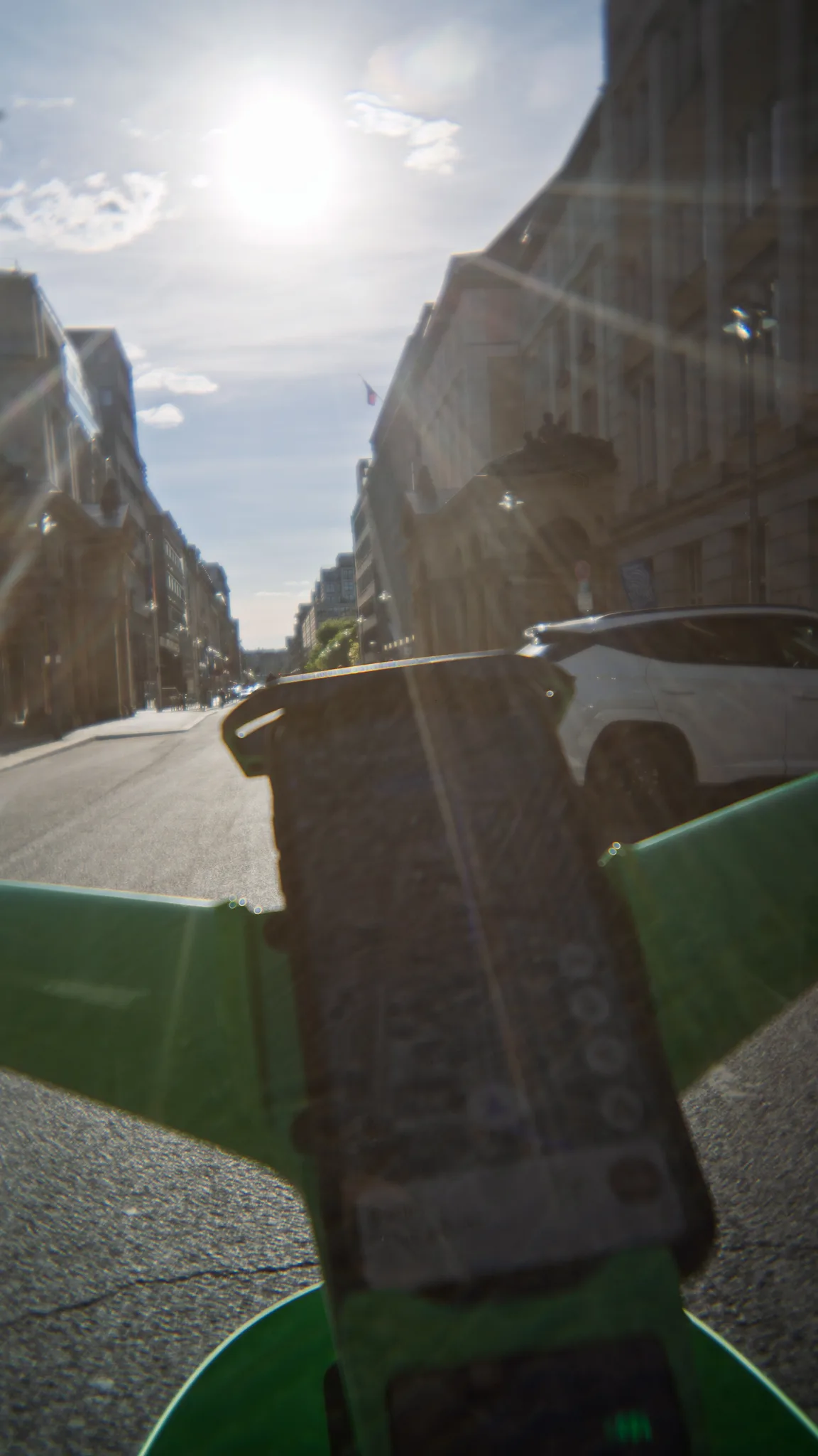 Looking down a sunlit Berlin street over the handlebars of a green hire bike