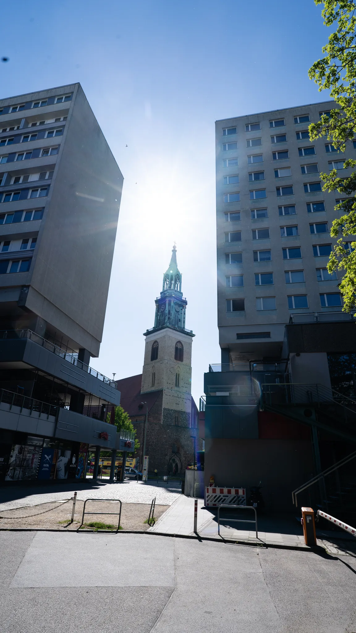 A church spire framed between two tower blocks, with the sun behind it